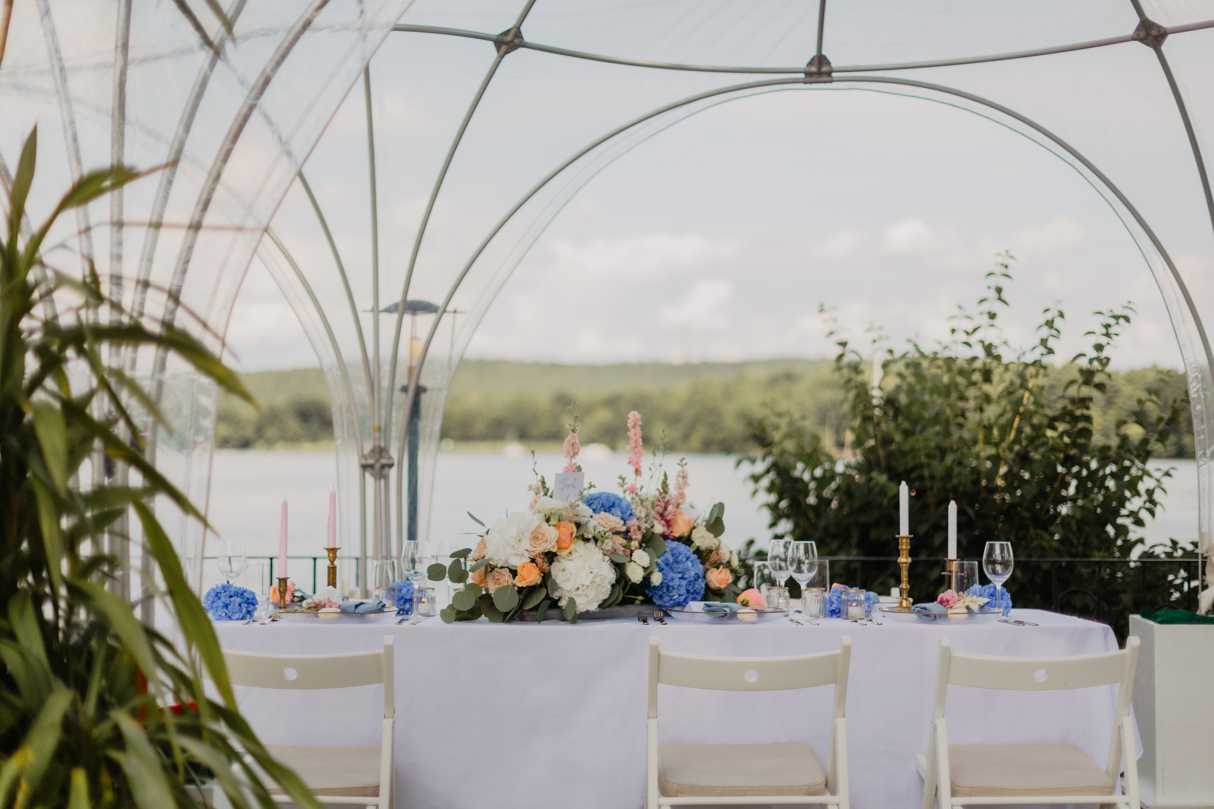 Gedeckte Hochzeitstafel unter heller Kuppel mit Blick auf den See.