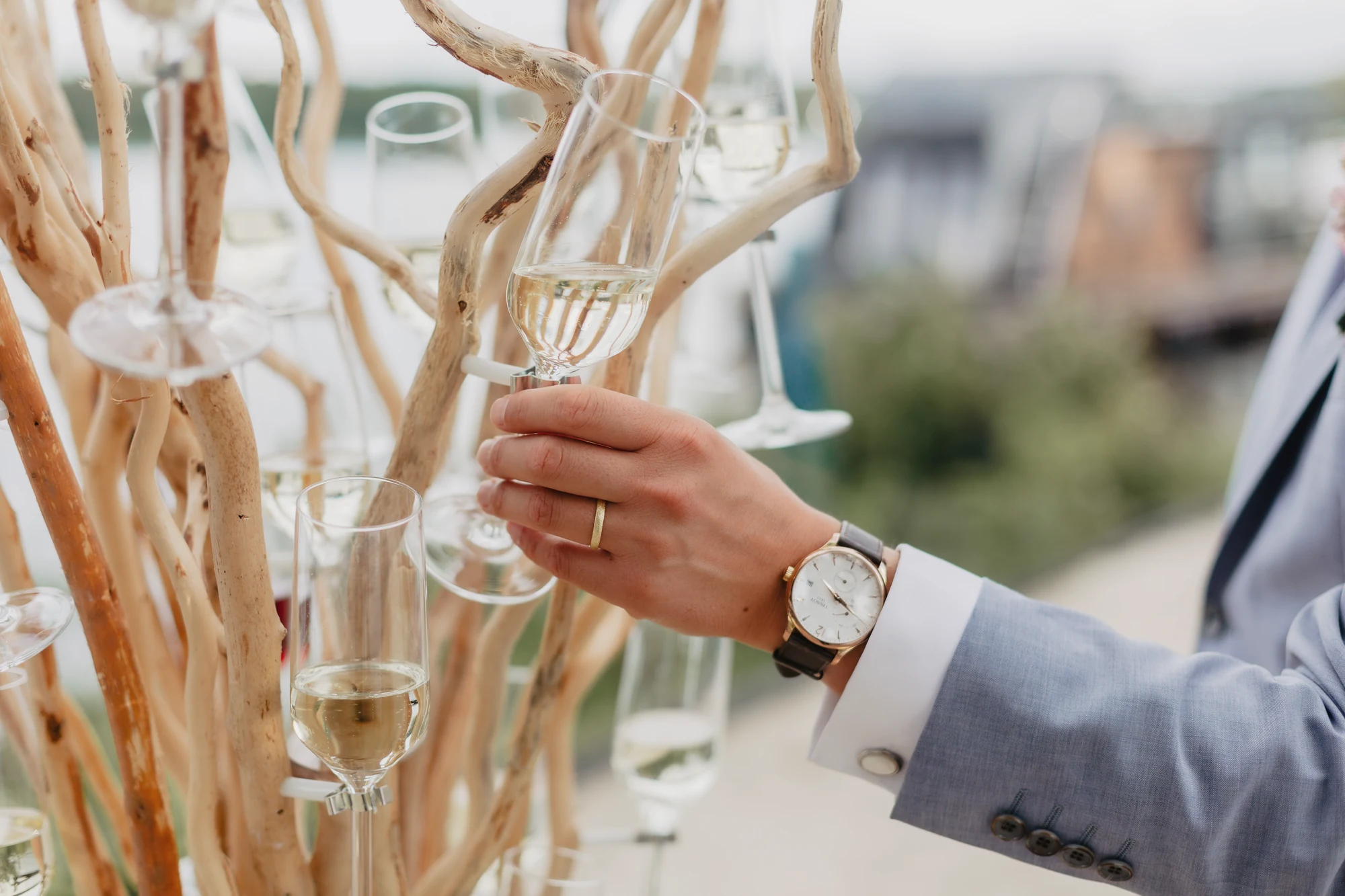 Hand nimmt ein Glas von einem Champagnerbaum mit See und Terrasse im Hintergrund.