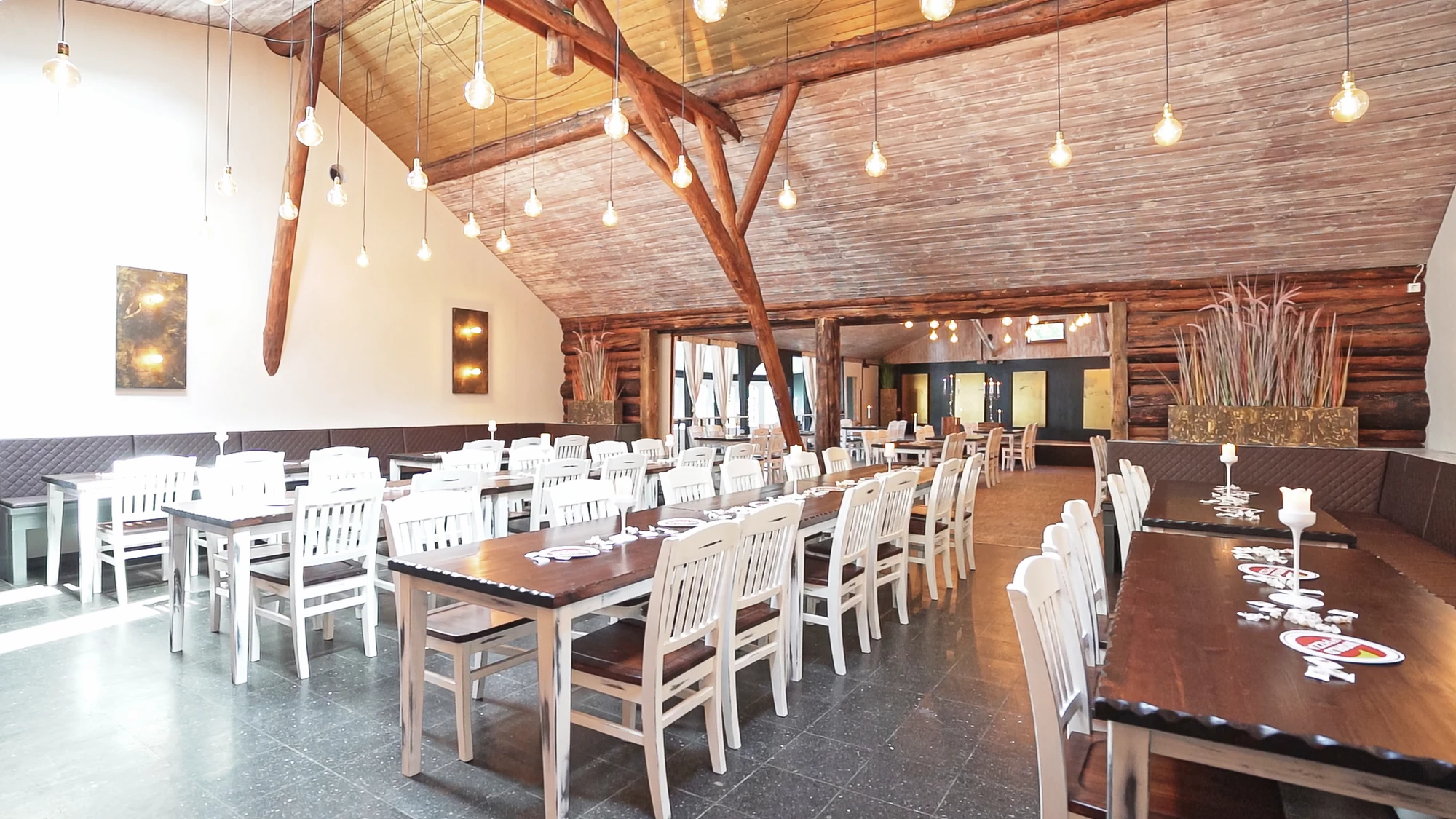 Heller Großer Saal mit Holzdach, weissen Stuehlen und gedeckten Tischen.