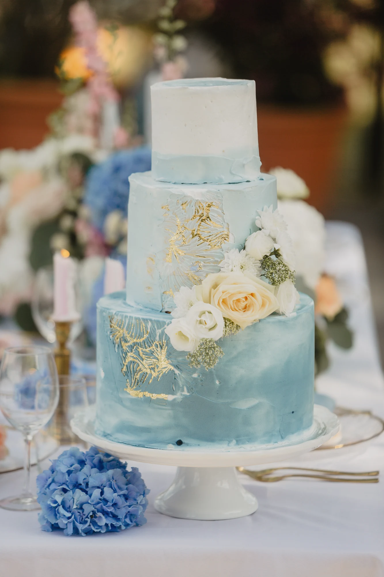 Blau-weisse Hochzeitstorte mit Blumen auf einer hell dekorierten Tafel.