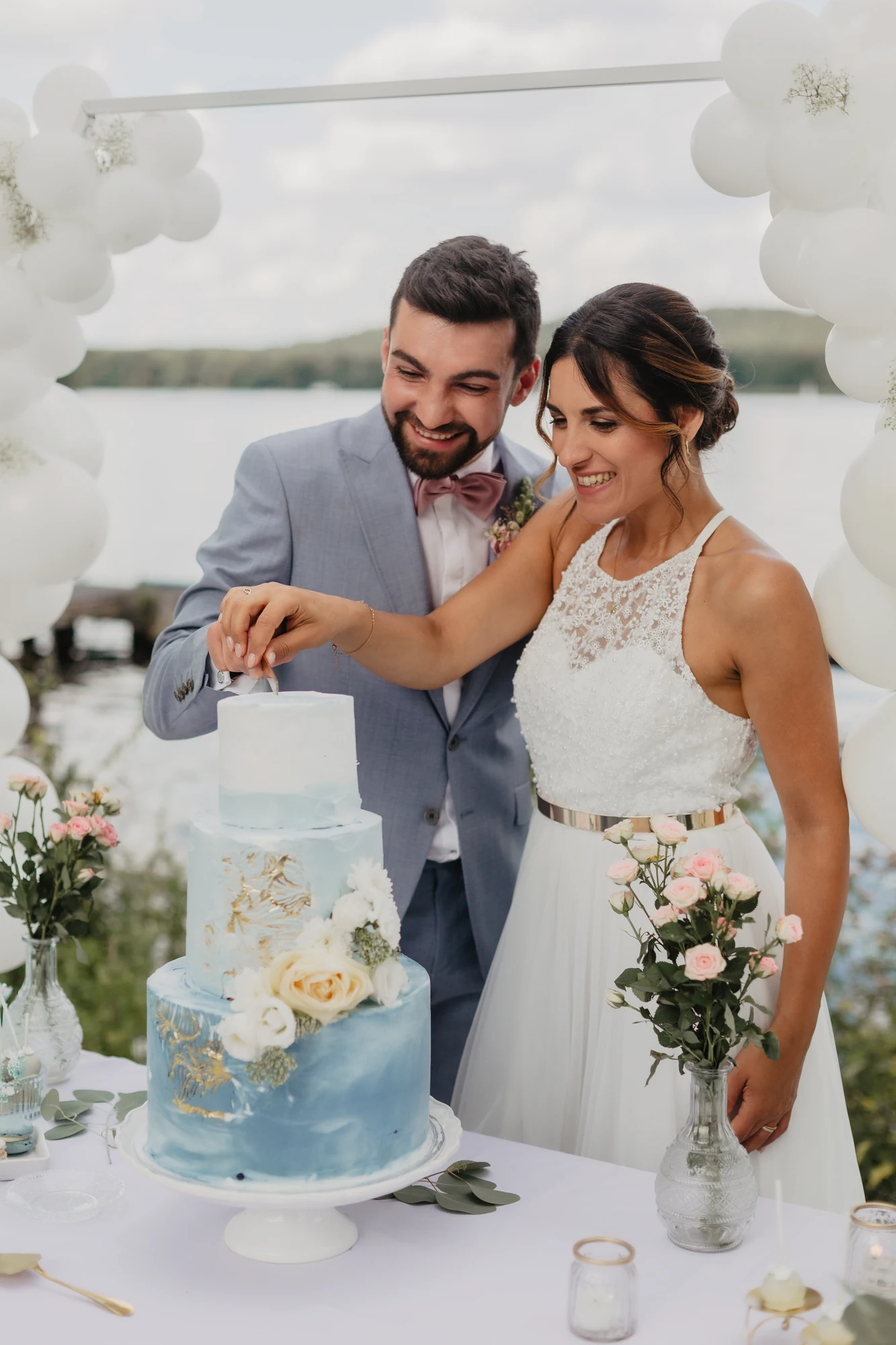 Brautpaar schneidet eine blau-weisse Hochzeitstorte vor Ballondeko an.