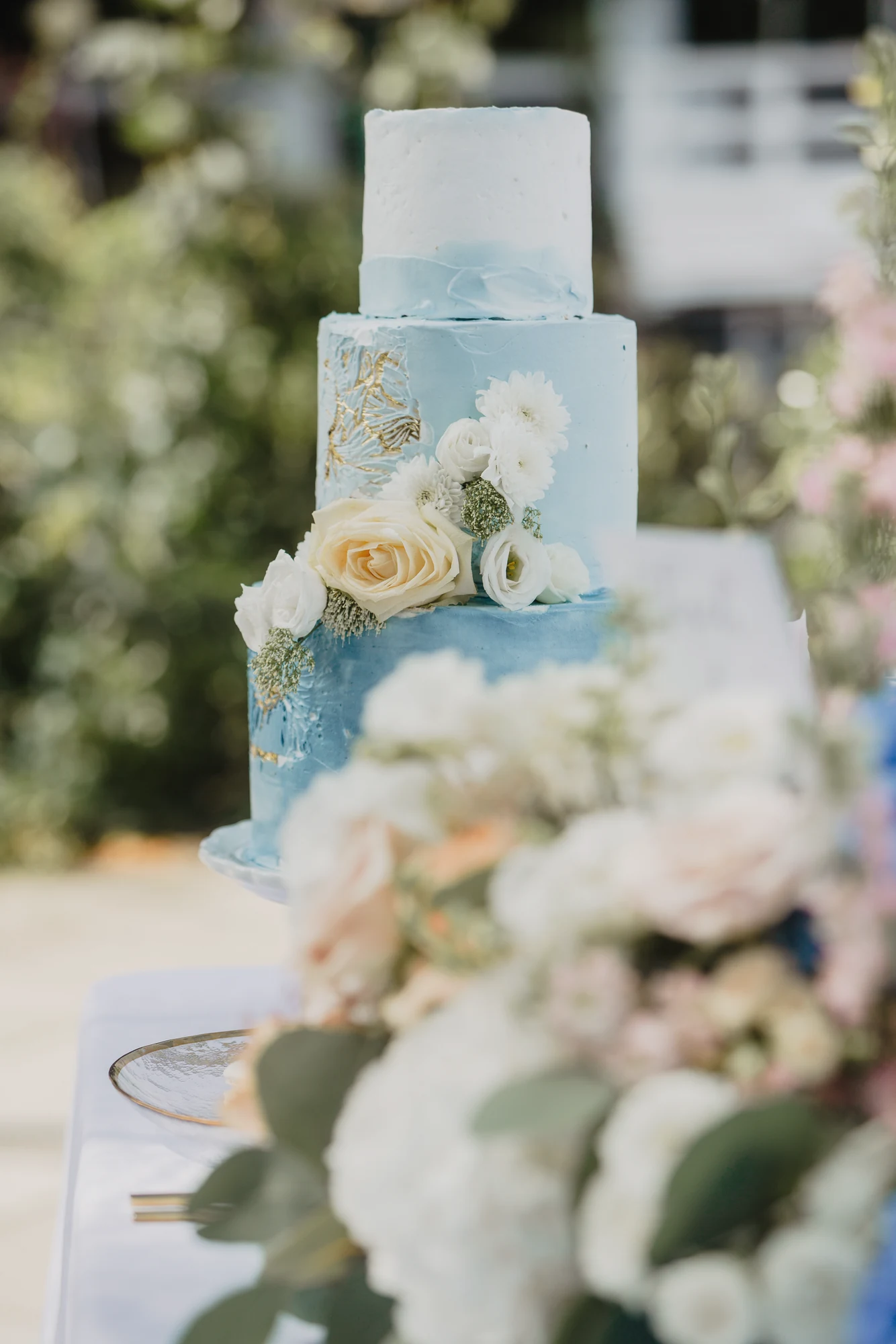 Mehrstoeckige blau-weisse Hochzeitstorte mit Blumen vor heller Dekoration.