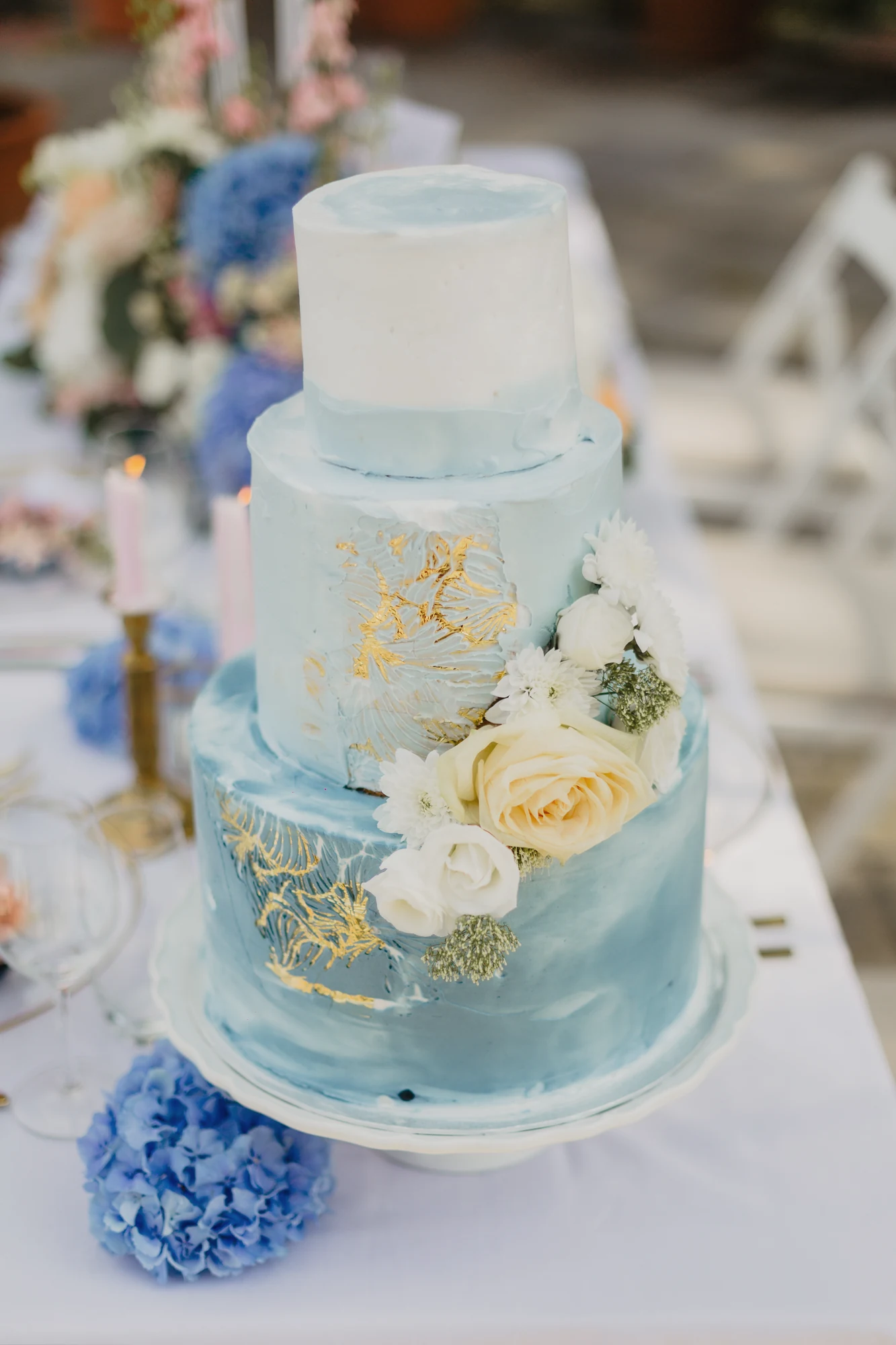 Blau-weisse Hochzeitstorte mit goldenen Details und Blueden auf gedeckter Tafel.