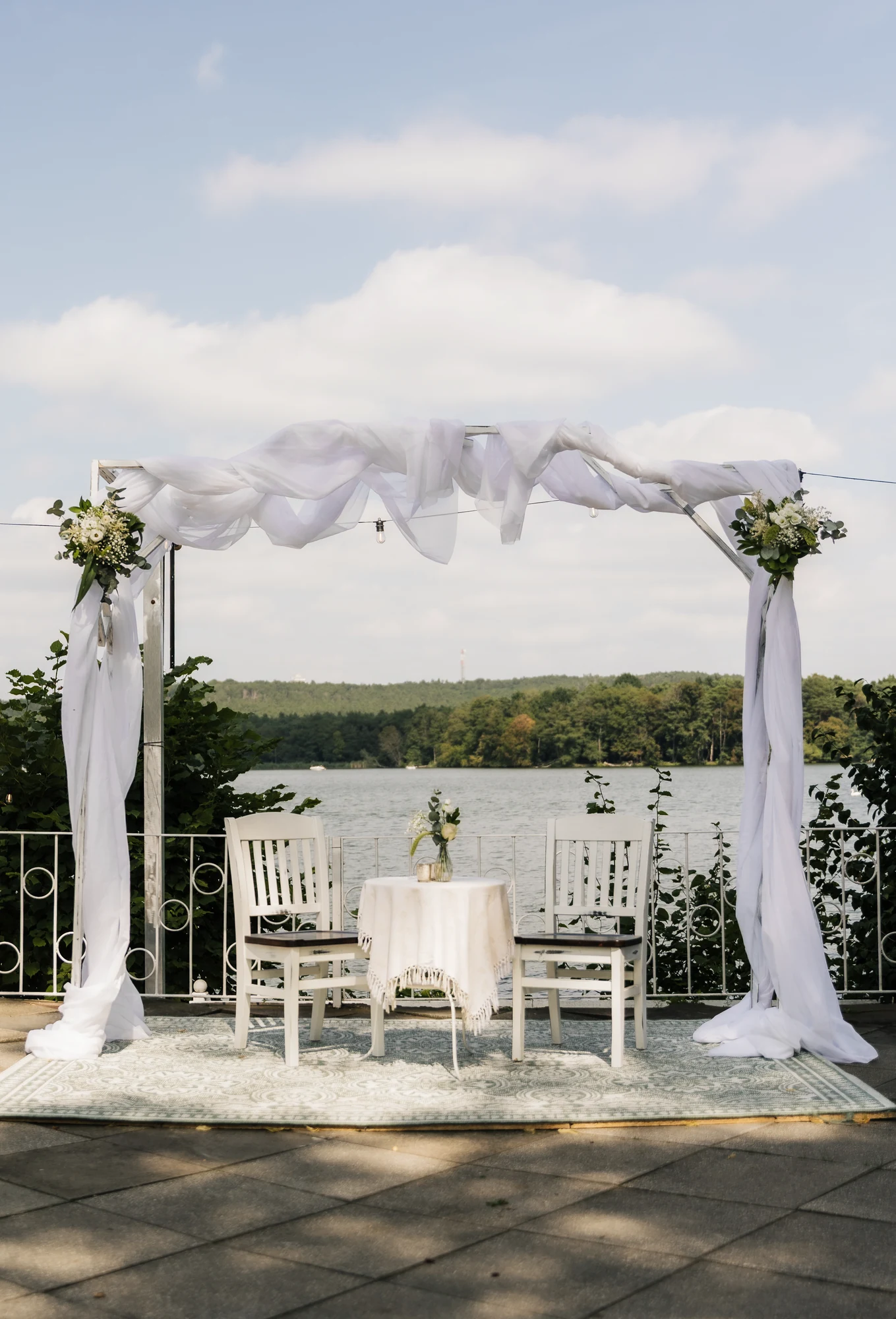 Freier Traubogen am See mit weissen Stuehlen fuer eine Hochzeit in Richtershorn.
