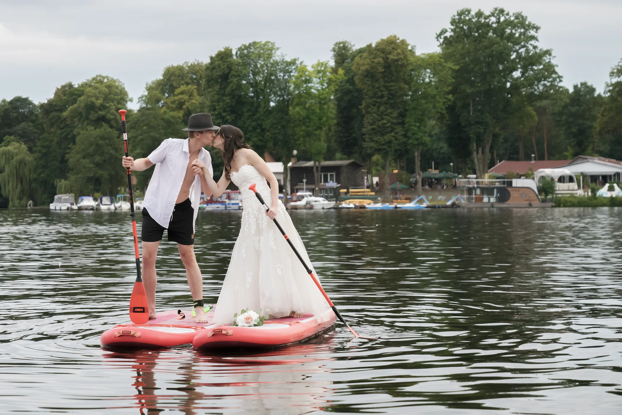 Brautpaar kuesst sich auf einem SUP-Board vor dem Seeufer.