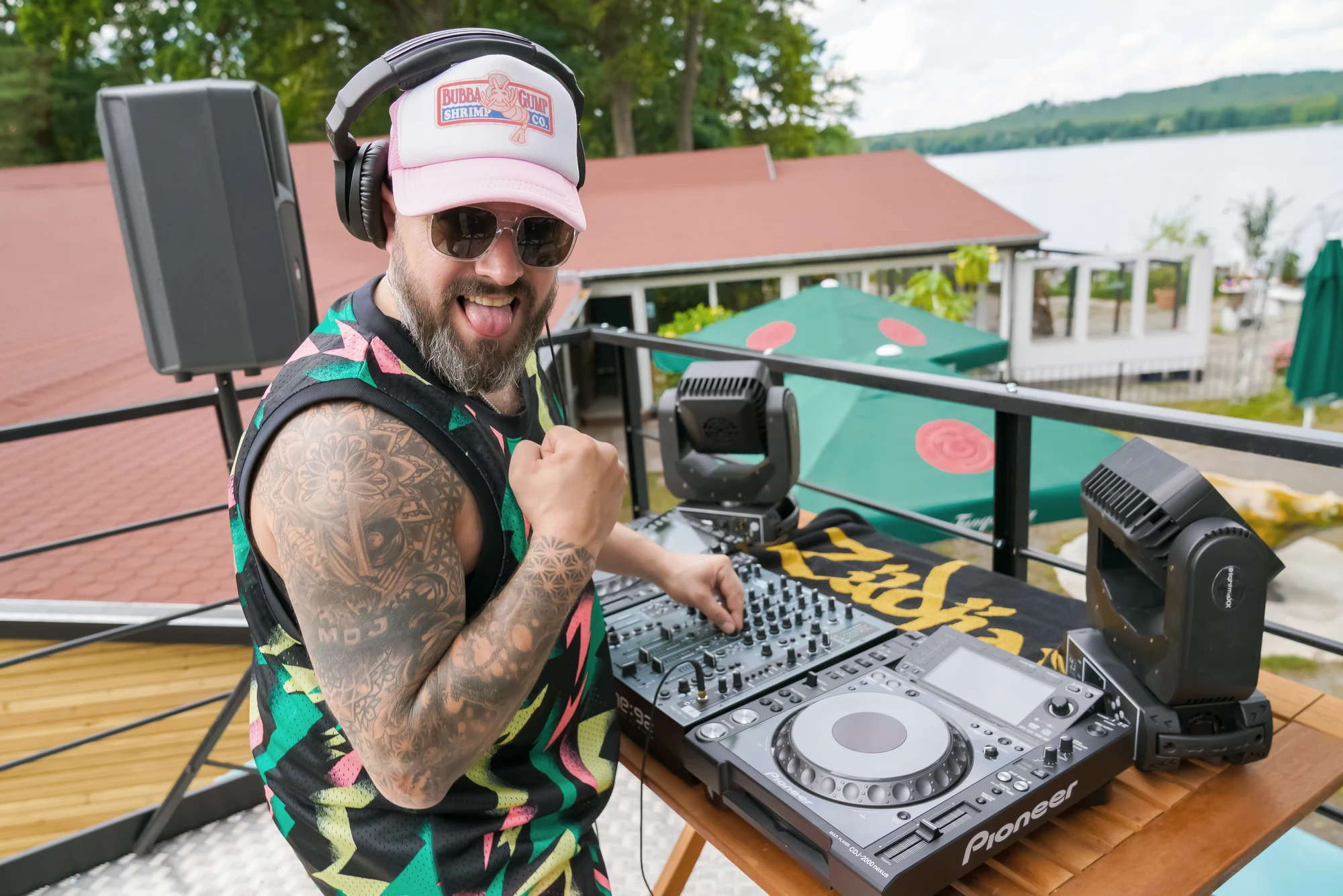DJ steht auf einem bunten Truck mit Technik, See und Terrasse im Hintergrund.