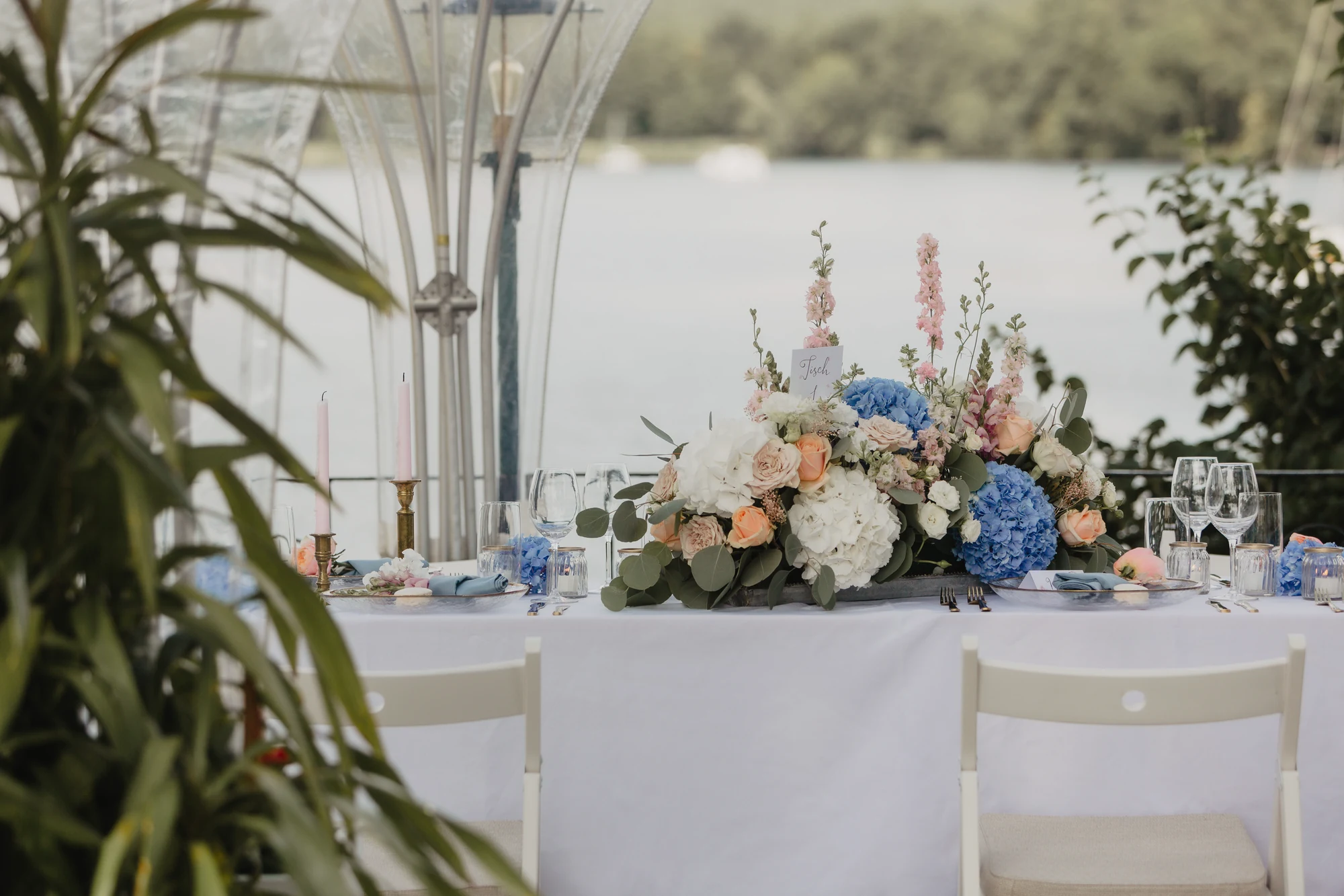 Gedeckte Tafel unter heller Kuppel mit Blumen und Blick auf den See.