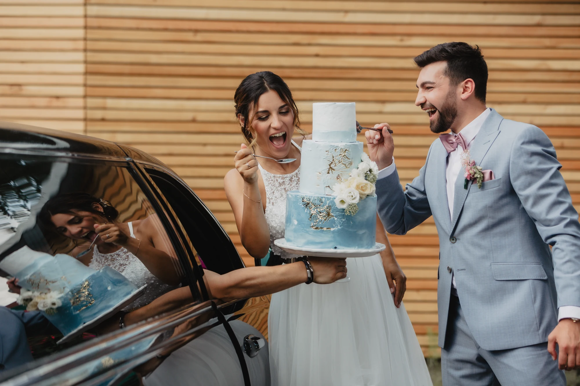 Brautpaar nimmt eine blaue Hochzeitstorte aus einem Auto vor der Location entgegen.