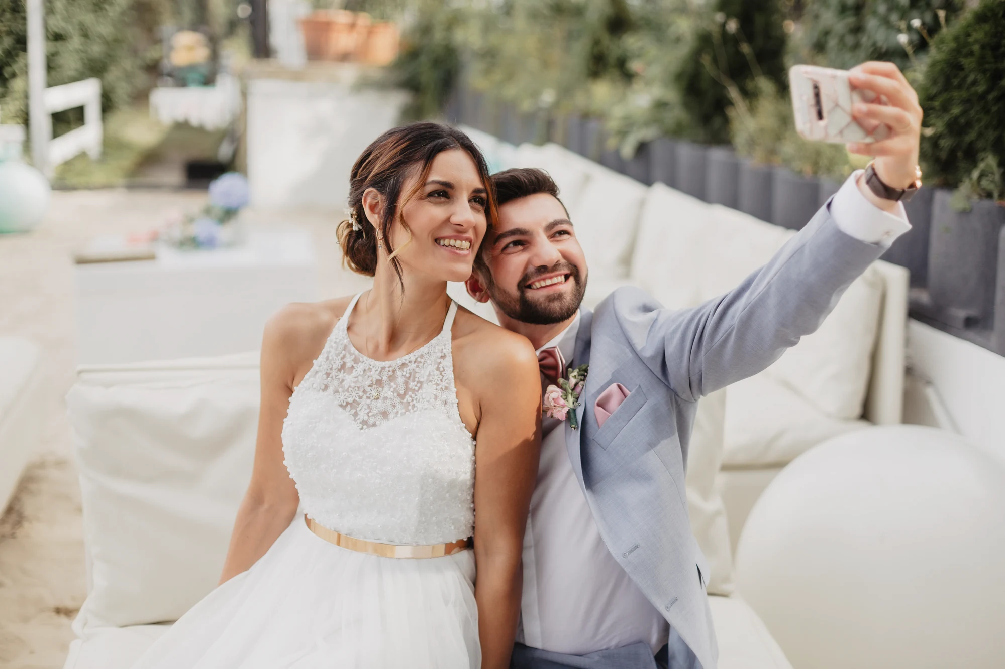 Brautpaar macht ein Selfie auf der Terrasse vor weisser Dekoration am See.