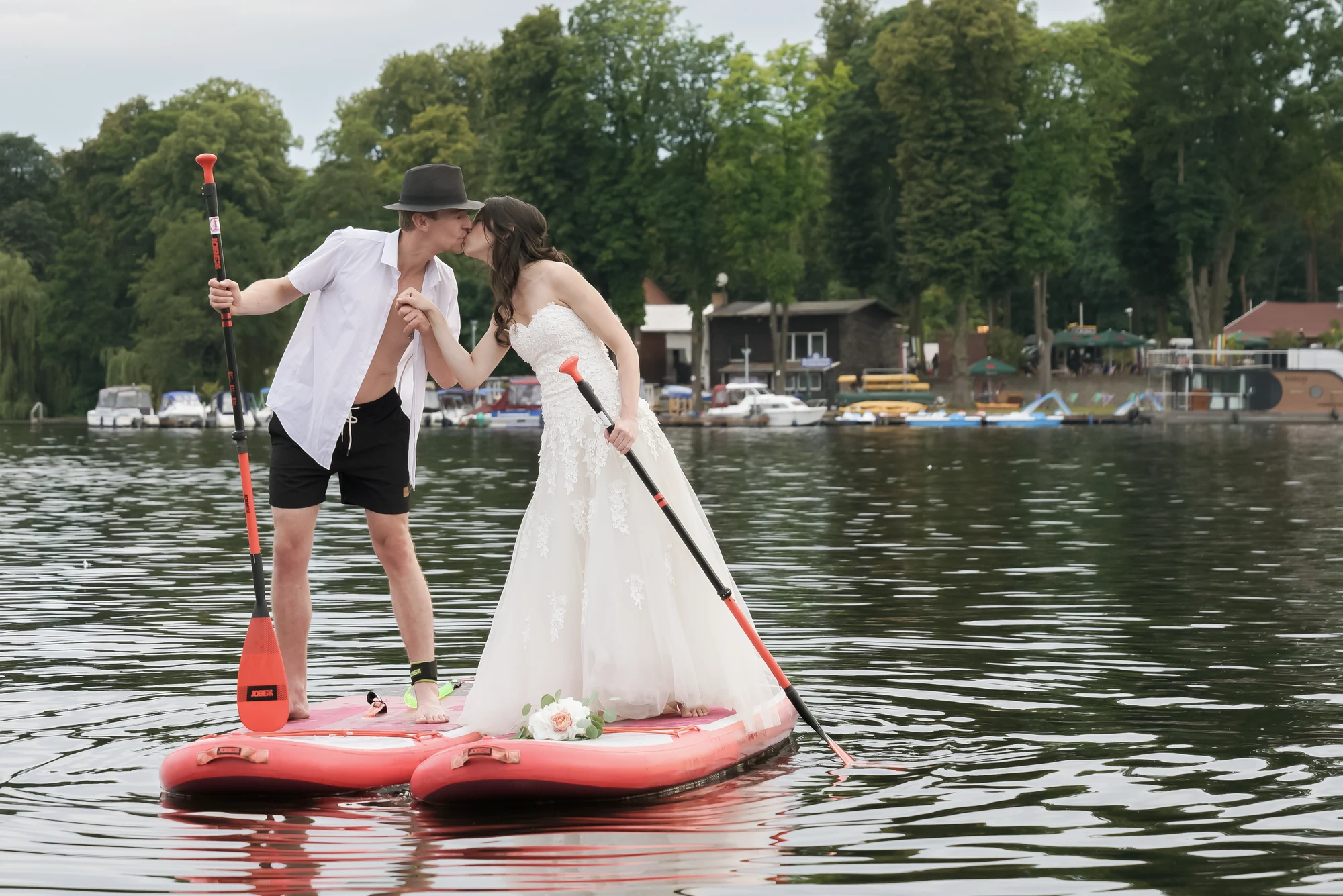 Brautpaar balanciert kussend auf einem SUP-Board im See vor der Location.