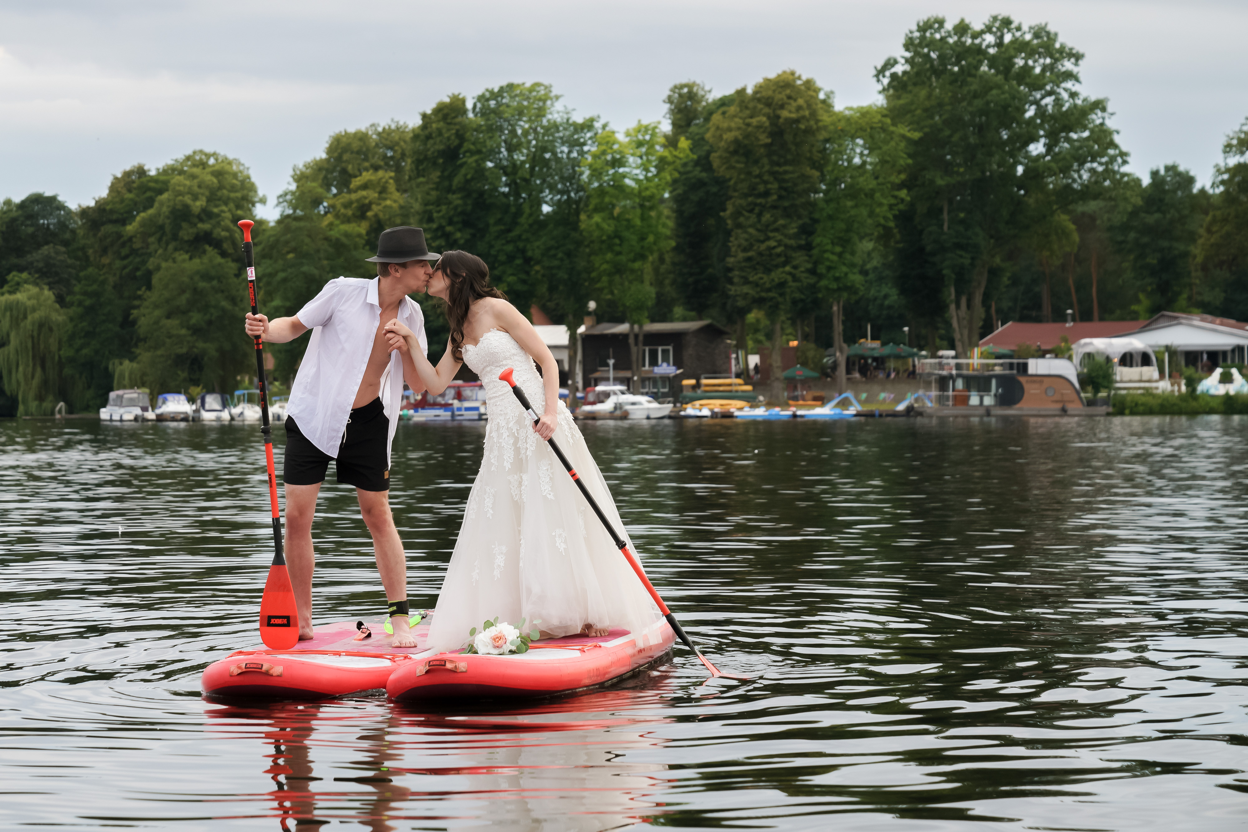 Brautpaar kuesst sich auf einem SUP-Board vor dem Seeufer.
