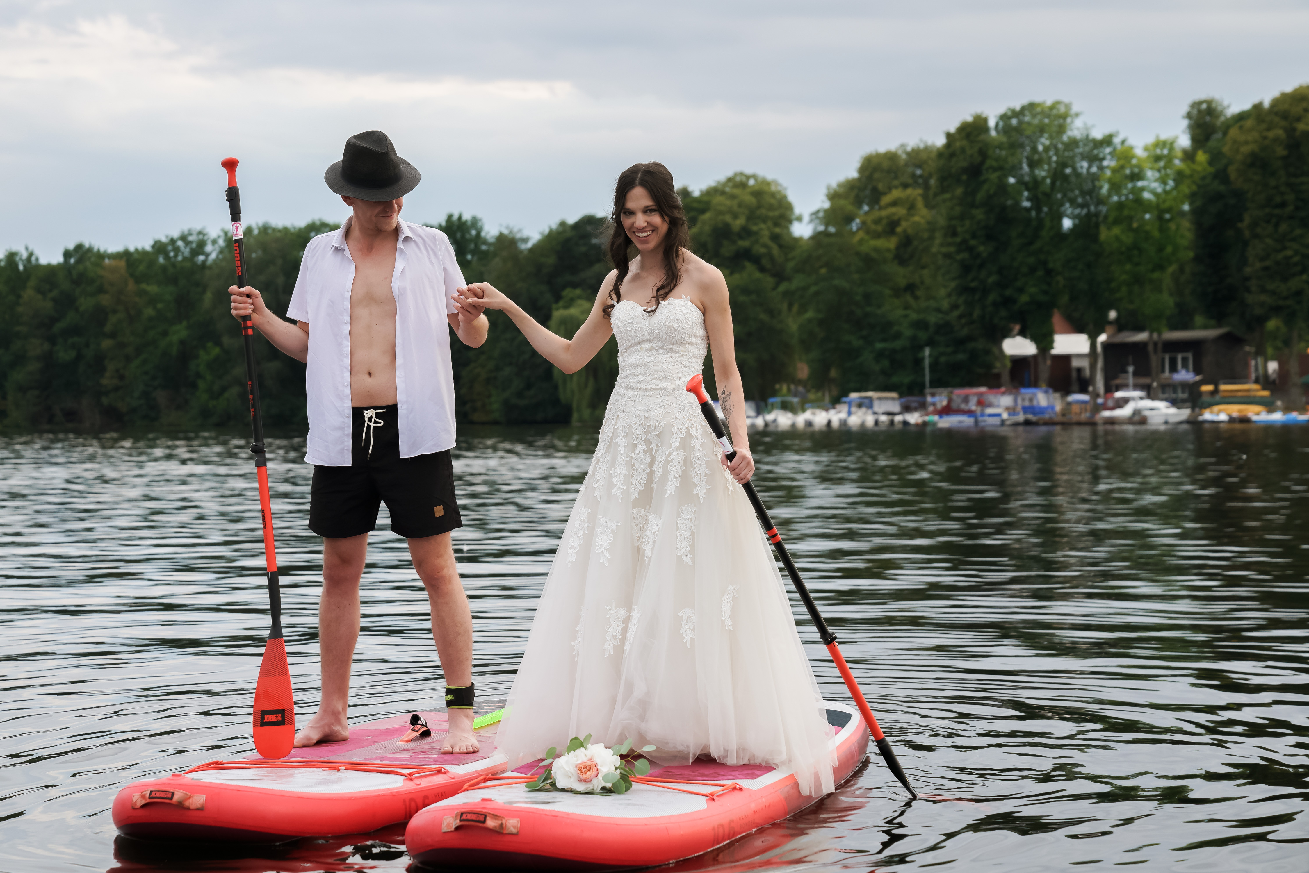 Brautpaar steht lachend mit Paddel auf einem SUP-Board auf dem See.